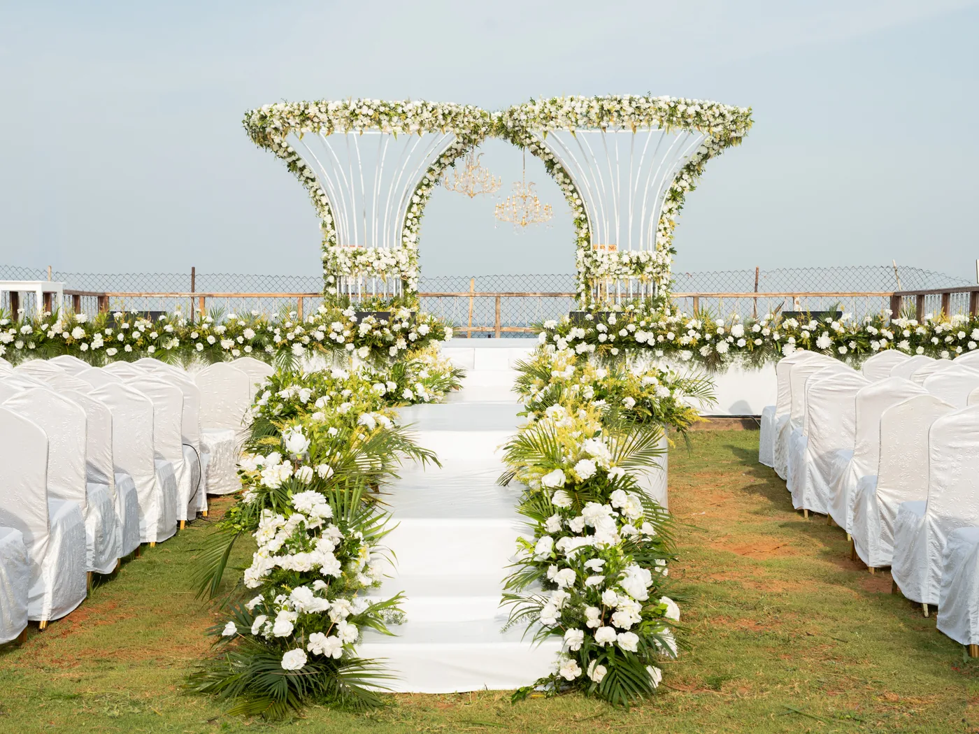 White carpeted aisle and steps lined with white flowers and palm leaves, leading up to the ceremony stage