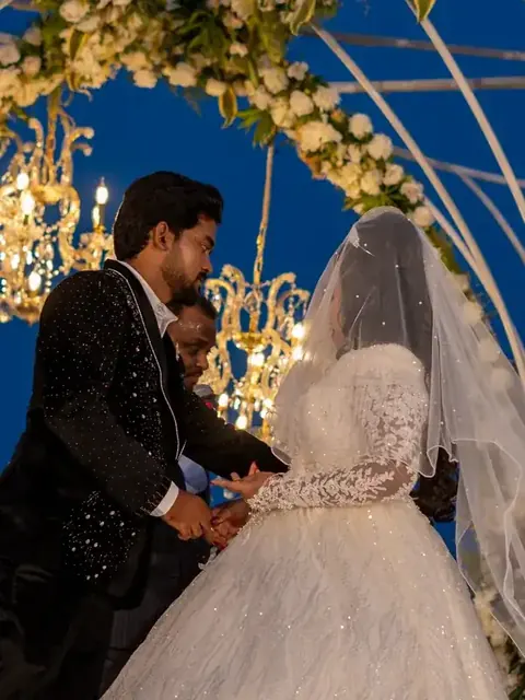 Couple beneath a floral arch hung with crystal chandeliers at night