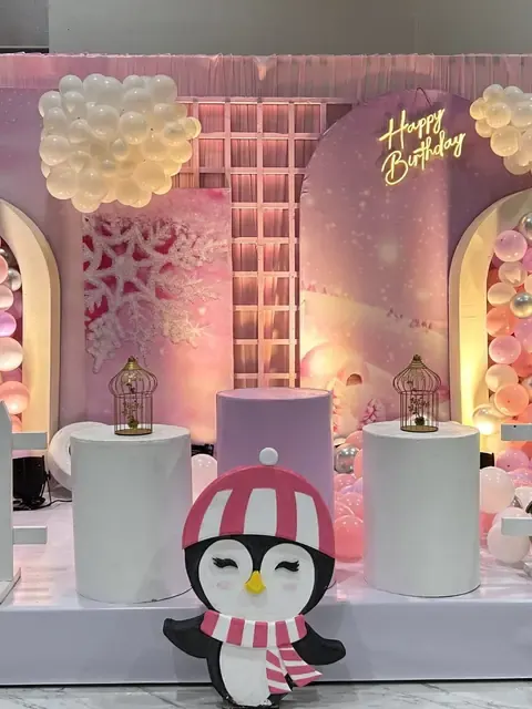 Pink penguin themed birthday stage with balloon arches